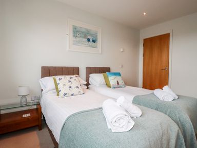 A bedroom with two single beds rolled towels on each bed and a wooden door in the background at Fistral Pearl in Newquay