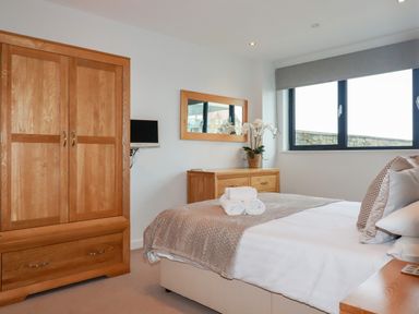 A bedroom with a wooden wardrobe a bed with folded towels and a dresser with a plant at Fistral Pearl in Newquay