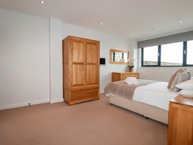 A bedroom with a bed pillows wardrobe chest of drawers and a window at Fistral Pearl in Newquay