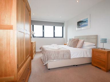 A bedroom with a bed pillows and wooden furniture including a wardrobe and bedside tables at Fistral Pearl in Newquay