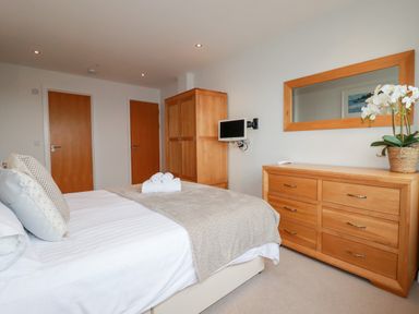 A bedroom with a bed pillows and blanket a wooden wardrobe a dresser with mirror and a small TV at Fistral Pearl in Newquay