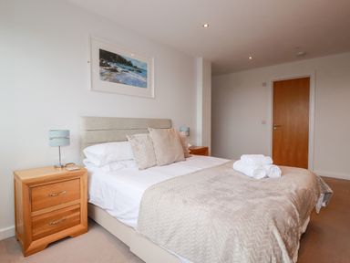 A bedroom with a bed and two wooden bedside tables with lamps at Fistral Pearl in Newquay