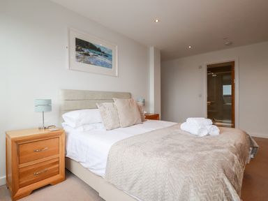 A bedroom with a bed pillows bedside tables lamps and a bathroom door at Fistral Pearl in Newquay