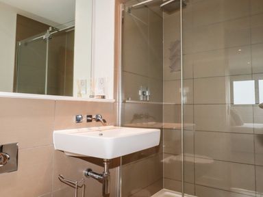 A bathroom with a wall mounted sink and a glass enclosed shower at Fistral Pearl in Newquay