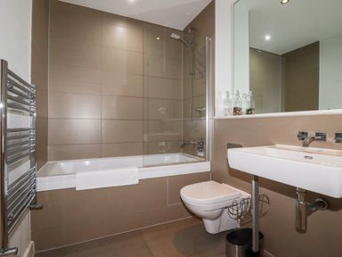 A bathroom with a bathtub shower combination a wall-mounted toilet and a sink with a large mirror at Fistral Pearl in Newquay