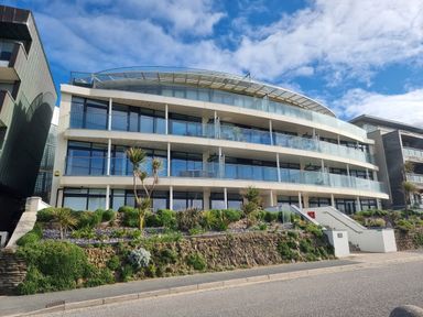 A modern apartment building with glass balconies and landscaped gardens in front at Fistral Pearl in Newquay