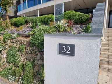 An outdoor area with a white wall displaying the number 32 stone steps and green plants at Fistral Pearl in Newquay
