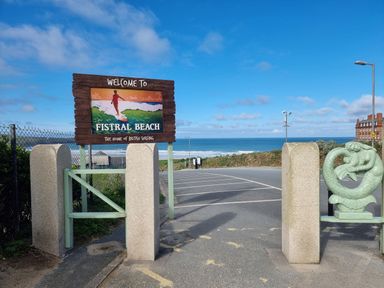 An entrance gate with a welcome sign for Fistral Beach and view of the sea and parking area at Fistral Pearl in Newquay