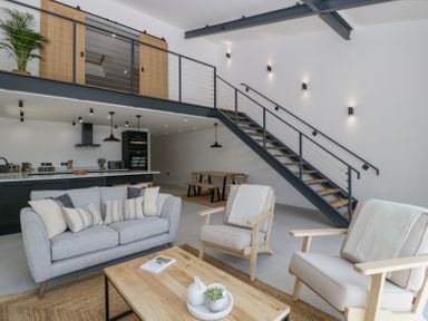 A living room with sofa and armchairs next to a wooden coffee table and a dining area under a staircase at Basswood Barn in Lime Tree Barn