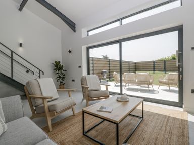A living room with two armchairs a coffee table and a sofa next to large sliding glass doors leading to a patio at Basswood Barn in Lime Tree Barn