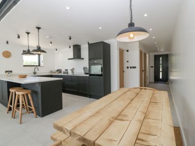 A kitchen with black cabinets an island with wooden stools and a wooden dining table at Basswood Barn in Lime Tree Barn
