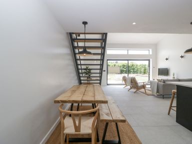 A dining area with wooden table and bench next to a staircase in an open living space with chairs and a sofa at Basswood Barn in Lime Tree Barn