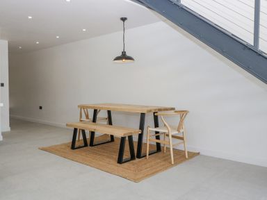 A dining area with a wooden table bench and chairs on a rug under a staircase at Basswood Barn in Lime Tree Barn