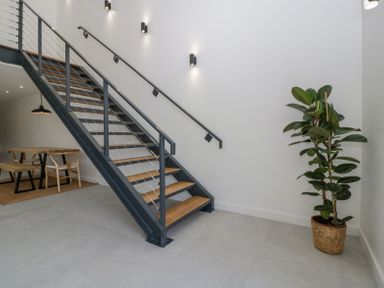A staircase with metal railing and wooden steps next to a dining area with wooden table and chairs and a potted plant at Basswood Barn in Lime Tree Barn