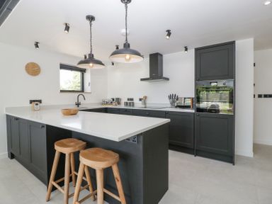 A kitchen with black cabinets white countertop two wooden stools pendant lights and a window at Basswood Barn in Lime Tree Barn