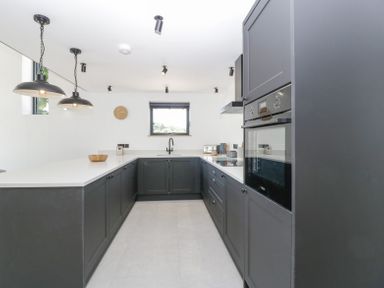 A kitchen with black cabinets white countertops and a small window at Basswood Barn in Lime Tree Barn