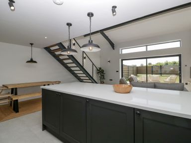 A kitchen island with a wooden bowl pendant lights dining table with benches and a staircase in an open plan living area at Basswood Barn in Lime Tree Barn