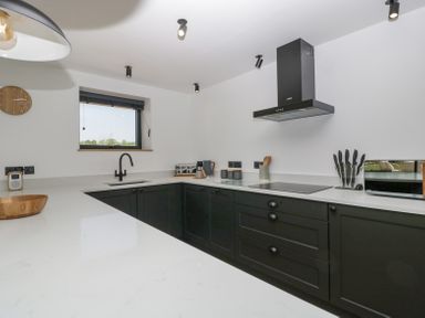 A kitchen with black cabinets a black faucet a stove with a black extractor fan knives in a holder and a toaster at Basswood Barn in Lime Tree Barn