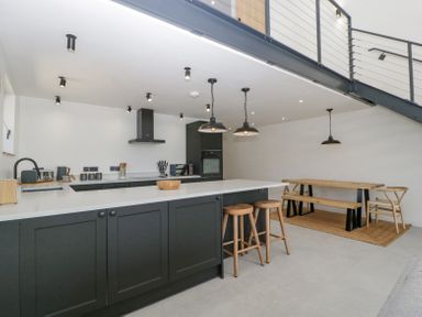 A kitchen with black cabinets a white countertop wooden stools and a wooden dining table at Basswood Barn in Lime Tree Barn