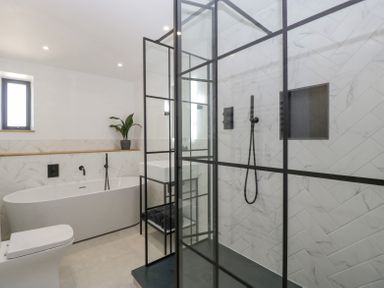 A bathroom with a bathtub, a toilet, a shower with glass panels, a sink, and a plant on a shelf at Basswood Barn in Lime Tree Barn