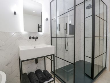 A bathroom with a white sink with black fixtures a black metal frame black towels and a glass shower enclosure with black frames at Basswood Barn in Lime Tree Barn