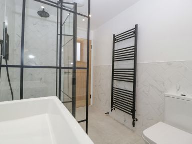A bathroom with a glass shower enclosure a black towel radiator a toilet and a white sink at Basswood Barn in Lime Tree Barn