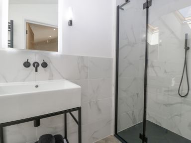 A bathroom with a rectangular sink on a black metal stand and a glass shower enclosure with black fixtures at Basswood Barn in Lime Tree Barn