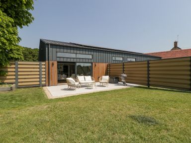 An outdoor patio with seating and a barbecue grill in a fenced backyard at Basswood Barn in Lime Tree Barn