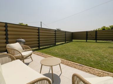 A patio with outdoor seating and a barbecue grill next to a grass lawn at Basswood Barn in Lime Tree Barn