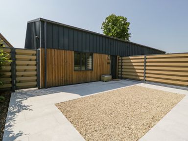 An outdoor area with a gravel section and tiled floor in front of a building with wooden and dark panels at Basswood Barn in Lime Tree Barn