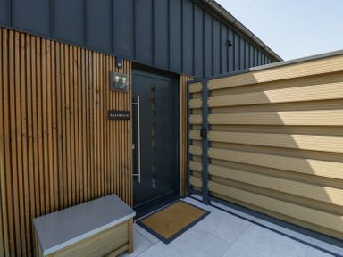 An entrance door with vertical wooden panels and a wooden fence at Basswood Barn in Lime Tree Barn