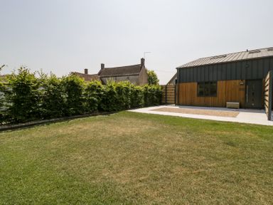 A garden with a lawn hedge and a building with wooden and metal exterior at Basswood Barn in Lime Tree Barn