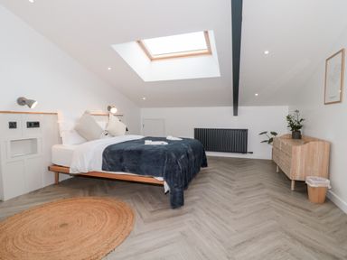 A bedroom with a bed under a skylight a wooden dresser and a round rug at Basswood Barn in Lime Tree Barn