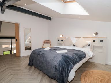 A bedroom with a bed with pillows and a blanket two wall lamps a wooden chair and a mirror at Basswood Barn in Lime Tree Barn