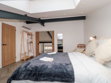 A bedroom with a bed a wooden door a wooden clothes rack and a wicker chair at Basswood Barn in Lime Tree Barn