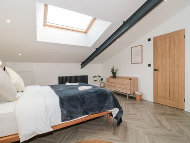 A bedroom with a bed under a skylight and a wooden dresser near a wooden door at Basswood Barn in Lime Tree Barn