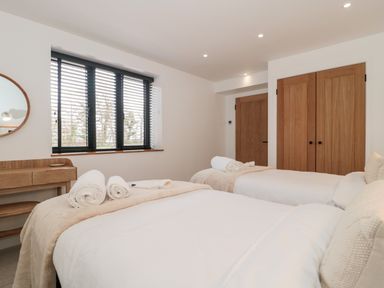 A bedroom with two beds white linens rolled towels on beds wooden doors and a wooden desk with a round mirror at Basswood Barn in Lime Tree Barn