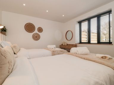 A bedroom with two beds and rolled towels on them a wall with woven baskets and a wooden vanity with mirror at Basswood Barn in Lime Tree Barn