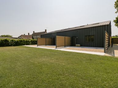 A modern dark-colored building with fenced patio areas and a lawn in front at Linden Barn in Wincanton