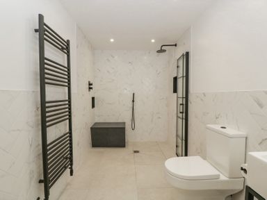 A bathroom with a toilet a black towel radiator a walk-in shower and a small sink at Linden Barn in Wincanton