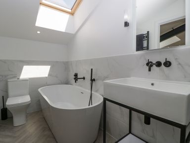 A bathroom with a bathtub toilet and sink under a skylight at Linden Barn in Wincanton