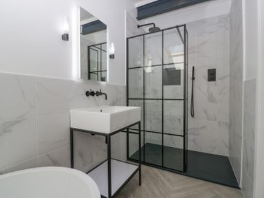 A bathroom with a walk-in shower with black framed glass panels a white sink with black metal stand and wall-mounted faucet and a round bathtub at Linden Barn in Wincanton