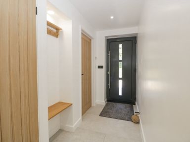 A hallway with wooden doors a black front door wooden bench and wall hooks at Linden Barn in Wincanton