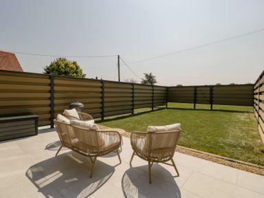 A patio with two chairs and a small table next to a lawn enclosed by a metal fence at Linden Barn in Wincanton