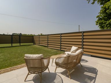 An outdoor patio with four cushioned chairs and a small table next to a grass yard and fencing at Linden Barn in Wincanton
