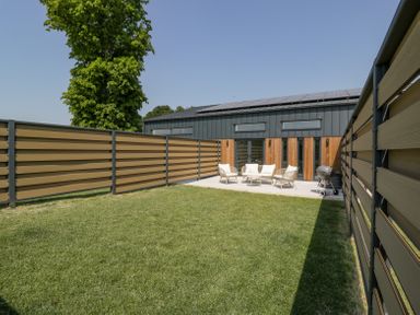 A fenced backyard with lawn chairs and a barbeque grill in front of a modern building at Linden Barn in Wincanton