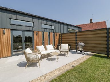 An outdoor patio with chairs a sofa table a grill and a wooden fence at Linden Barn in Wincanton