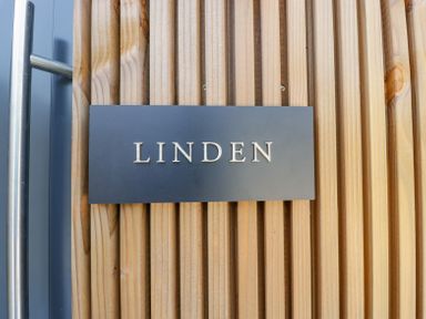 A black plaque with the word Linden mounted on vertical wooden slats next to a metal door handle at Linden Barn in Wincanton