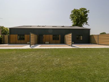 A modern building with metal and wood exterior panels surrounded by grass and partitioned walkways at Linden Barn in Wincanton