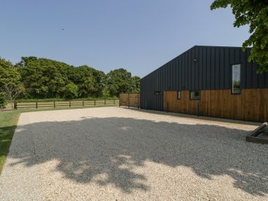 A gravel driveway next to a building with wooden and black exterior walls at Linden Barn in Wincanton
